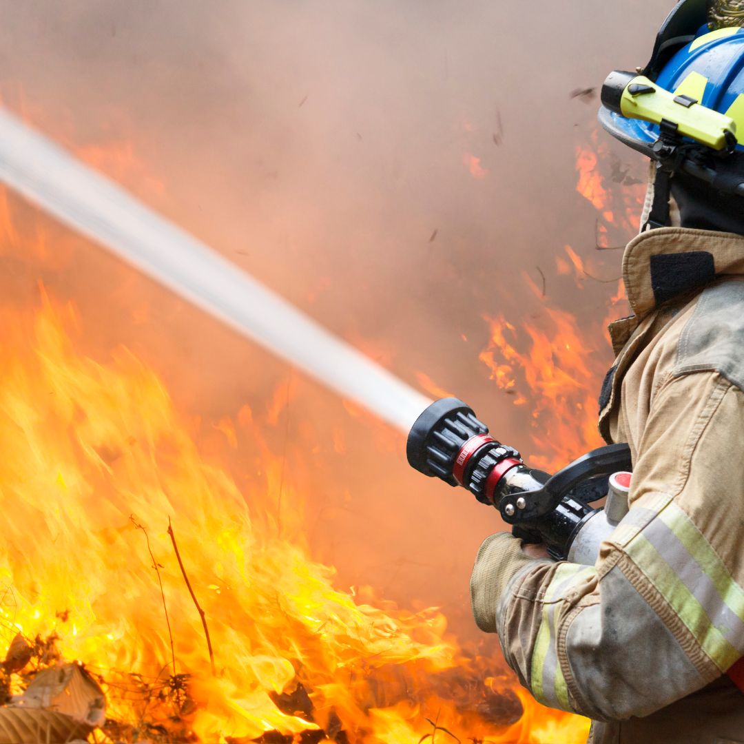 Fire fighter dousing wildfire blaze with water from hose