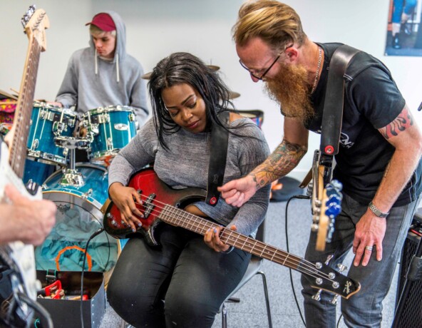 Young person being shown how to play a chord on an electric guitar